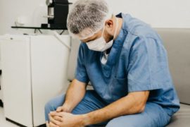 man-wearing-blue-scrub-suit-and-mask-sitting-on-bench-3279197